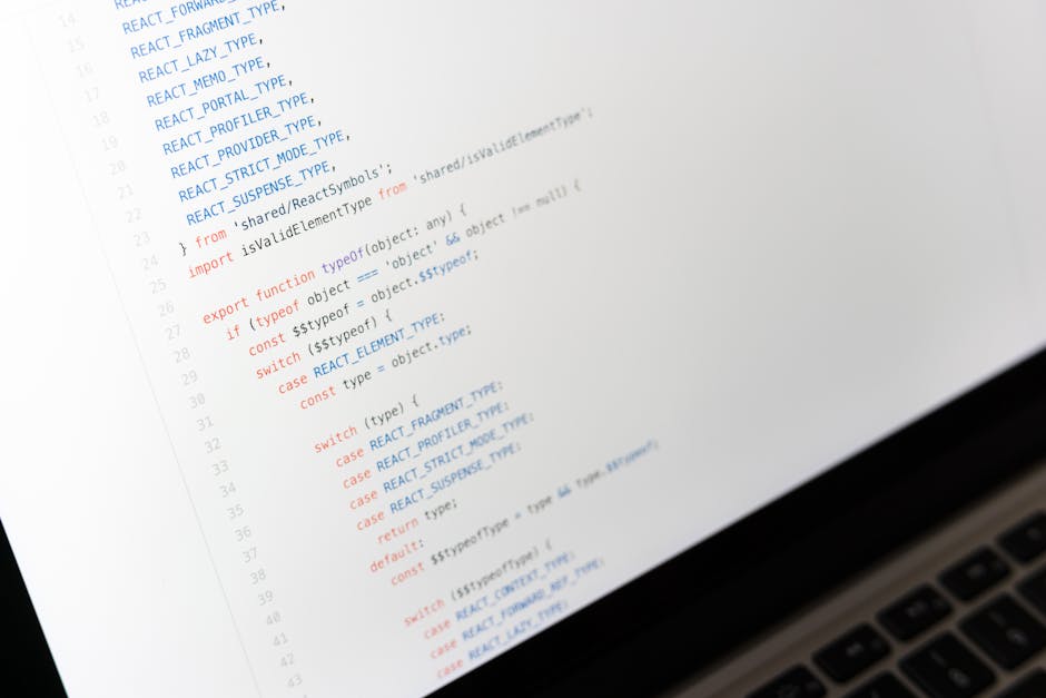 A close-up image of a computer screen displaying lines of code in a text editor, with syntax highlighting in blue, red, and black, and a laptop keyboard partially visible at the bottom right corner. T