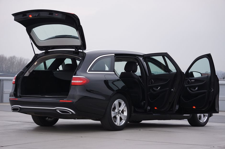 A sleek black estate car with all doors and the rear hatch open, parked on a grey rooftop under an overcast sky. The vehicle's interior and trunk space are visible, with no flowers or floral arrangeme